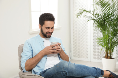 Young man with cup of drink relaxing at home