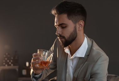 Photo of Young man with glass of whiskey at home. Space for text