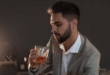 Young man with glass of whiskey at home. Space for text