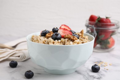 Photo of Tasty oatmeal with strawberries, blueberries and walnuts in bowl on white marble table