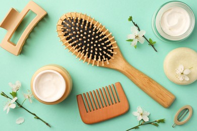 Flat lay composition with wooden hairbrush, comb and cosmetic products on turquoise background