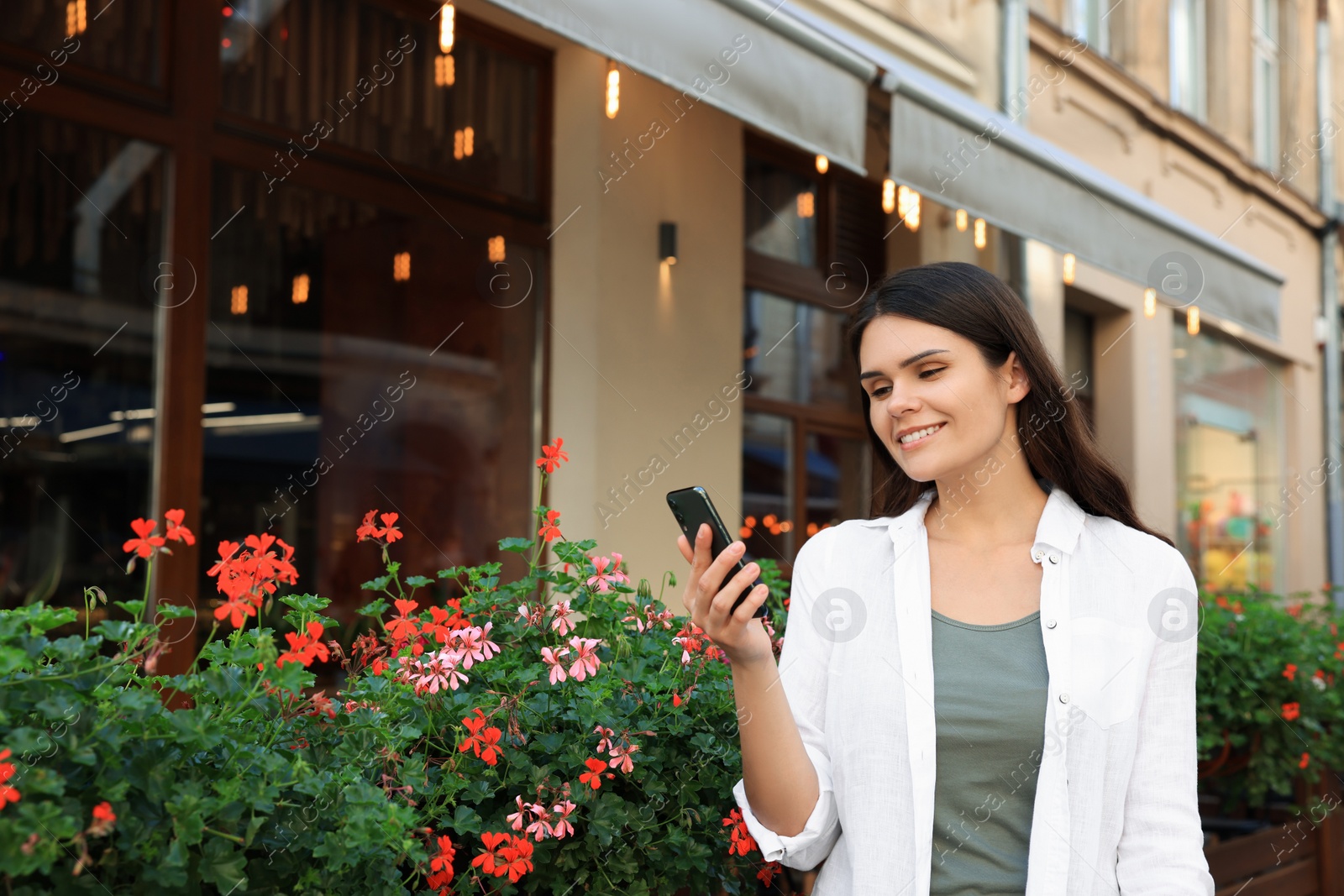 Photo of Young woman with smartphone near beautiful flowers on city street