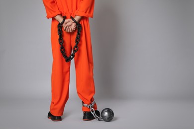 Prisoner in orange jumpsuit with chained hands and metal ball on grey background, closeup. Space for text