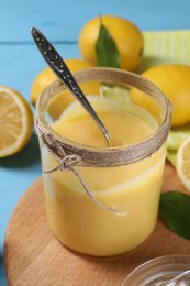 Delicious lemon curd in glass jar, fresh citrus fruits and spoon on light blue table, closeup