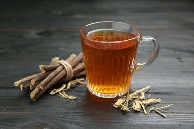 Aromatic licorice tea in cup and dried sticks of licorice root on black wooden table