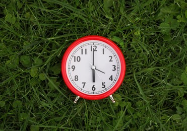Photo of Red alarm clock on green grass outdoors, top view