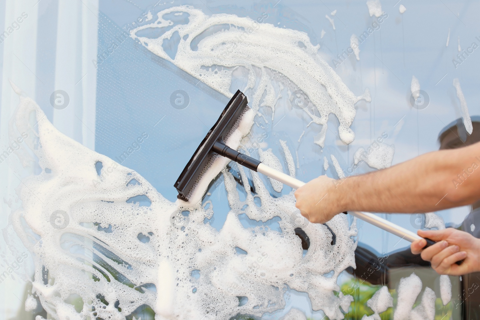 Photo of Male cleaner wiping window glass with squeegee from outside, closeup