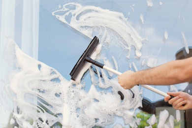 Photo of Male cleaner wiping window glass with squeegee from outside, closeup