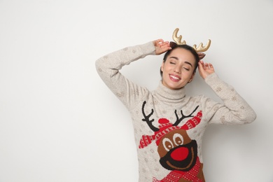 Photo of Young woman in Christmas sweater and deer headband on white background, space for text