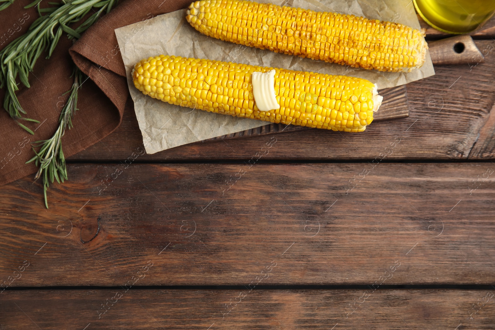 Photo of Fresh grilled corn cobs with butter on wooden table, flat lay. Space for text