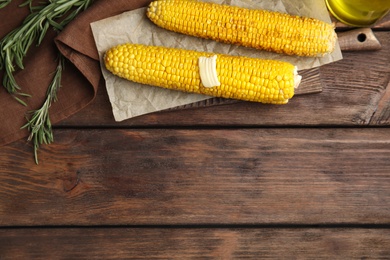 Fresh grilled corn cobs with butter on wooden table, flat lay. Space for text