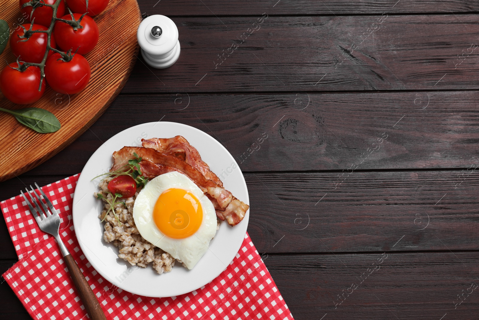 Photo of Tasty boiled oatmeal with fried egg, bacon and tomato served on wooden table, flat lay. Space for text