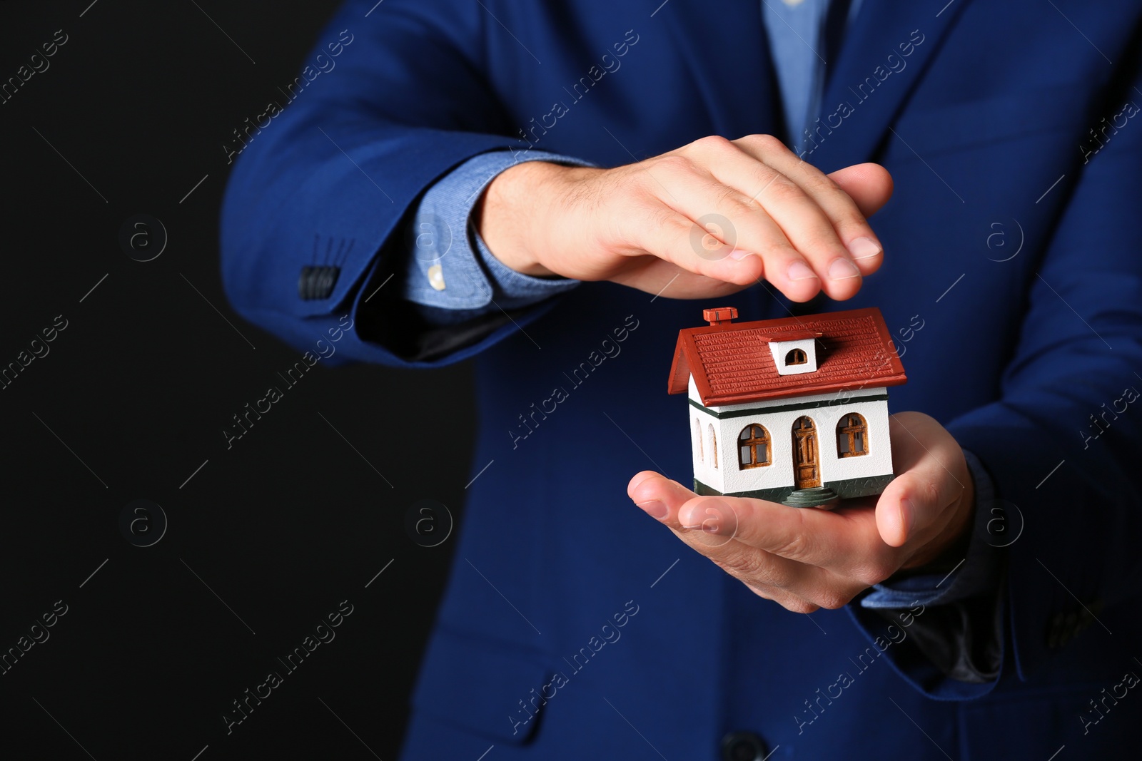 Photo of Male agent covering house model on black background, closeup. Home insurance