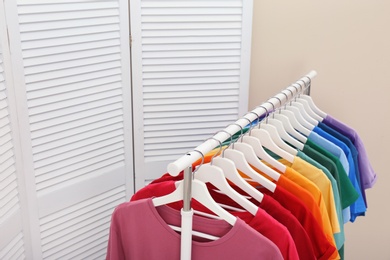 Photo of Rack with bright clothes in room. Rainbow colors