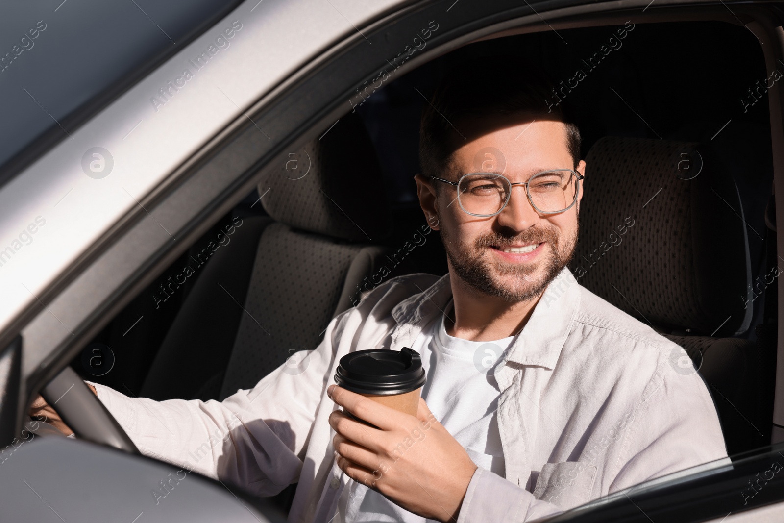 Photo of Coffee to go. Happy man with paper cup of drink in car