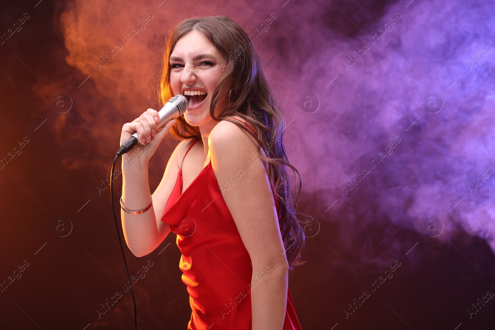 Photo of Emotional woman with microphone singing in color lights. Space for text