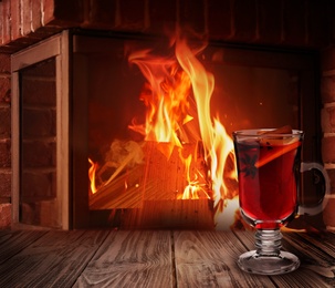 Mulled wine in glass cup on wooden table near fireplace