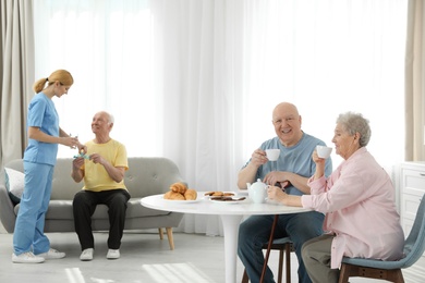 Photo of Nurse assisting elderly man while senior couple having breakfast at retirement home