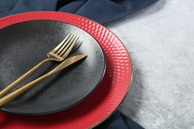 Elegant ceramic plates and cutlery on light textured table, closeup. Space for text