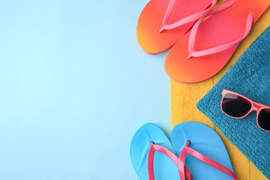 Photo of Flip flops, towels and sunglasses on light blue background, flat lay with space for text. Beach accessories