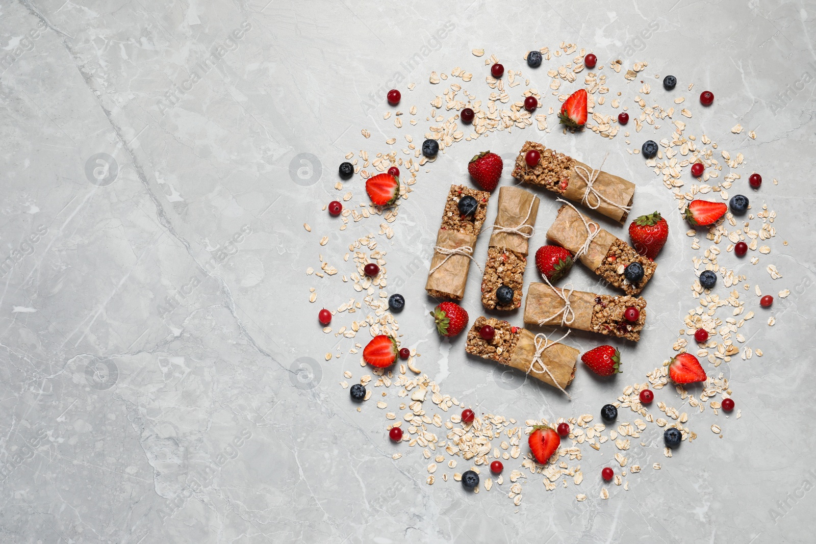 Photo of Tasty granola bars and ingredients on light grey marble table, flat lay. Space for text