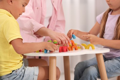 Photo of Little children and nursery teacher playing with colorful wooden pieces at desk in kindergarten, closeup. Playtime activities for motor skills development