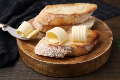 Photo of Tasty butter curls, knife and slices of bread on wooden table, closeup