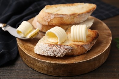 Tasty butter curls, knife and slices of bread on wooden table, closeup