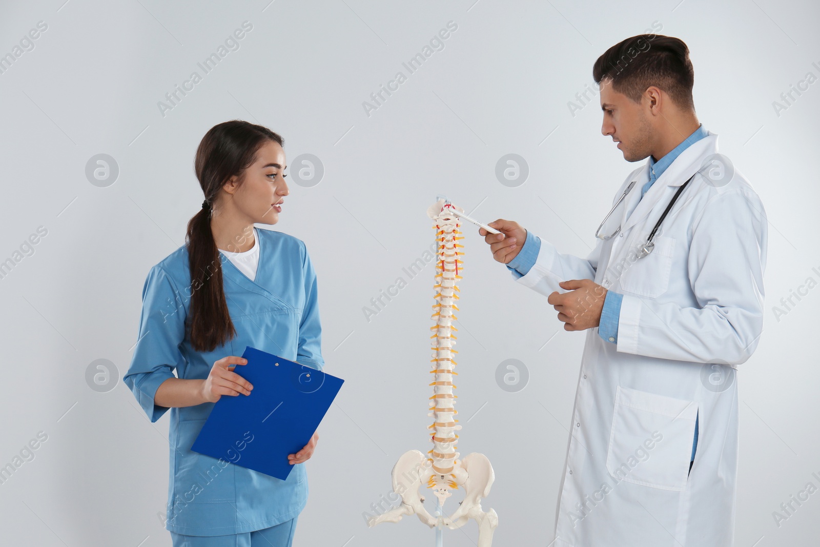 Photo of Professional orthopedist with human spine model teaching medical student against light background