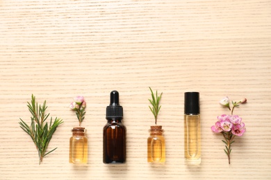 Flat lay composition with bottles of natural tea tree oil and space for text on wooden background