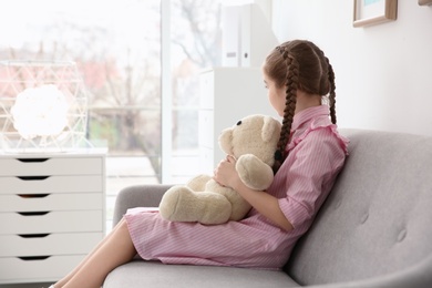 Photo of Little autistic girl sitting on sofa with toy at home