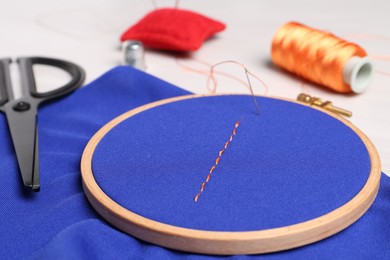 Photo of Blue cloth with stitches, sewing thread, needle and scissors on light table, closeup
