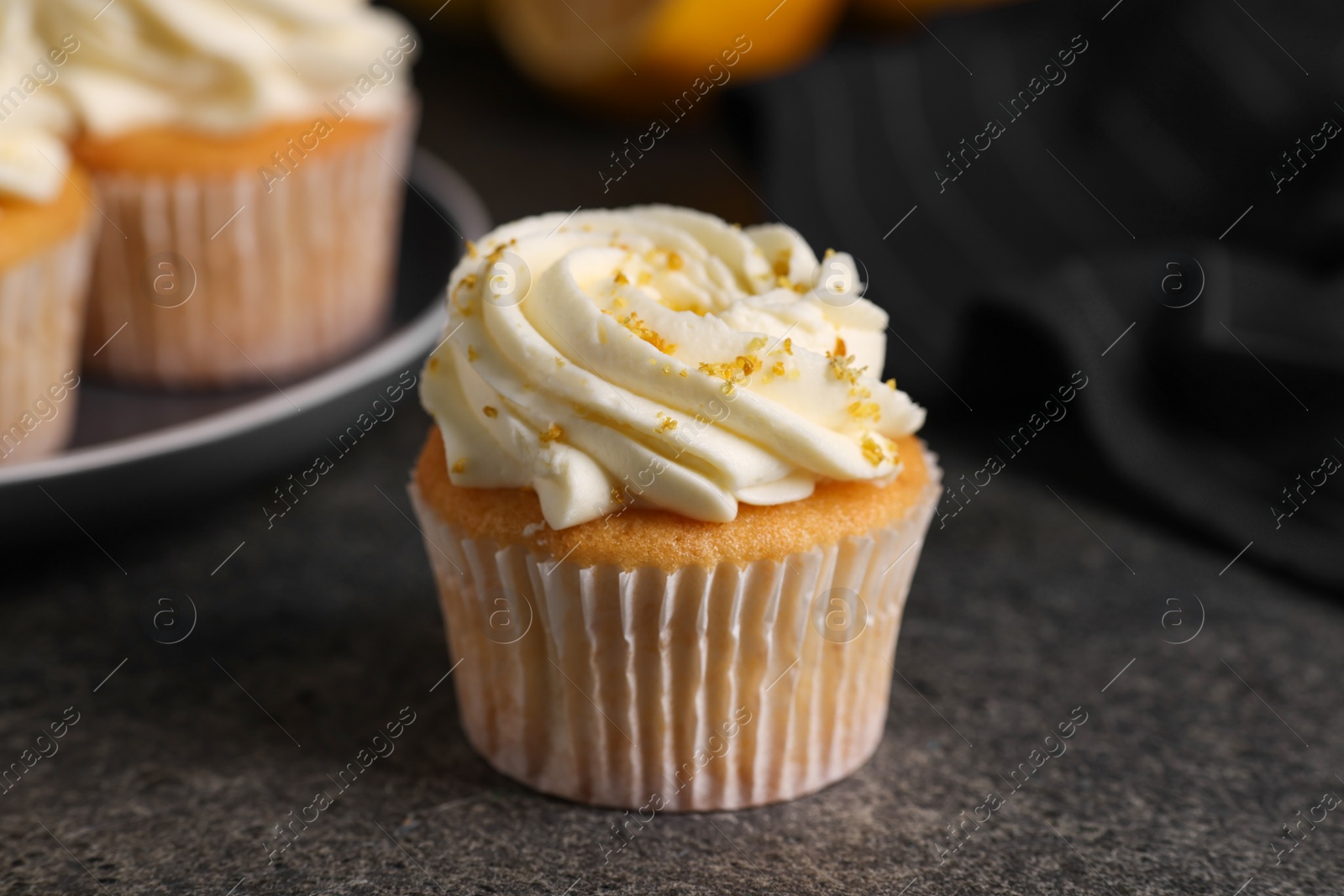 Photo of Delicious cupcake with white cream and lemon zest on gray table, closeup