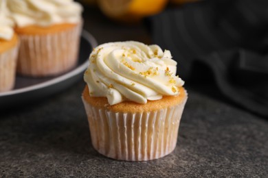 Delicious cupcake with white cream and lemon zest on gray table, closeup