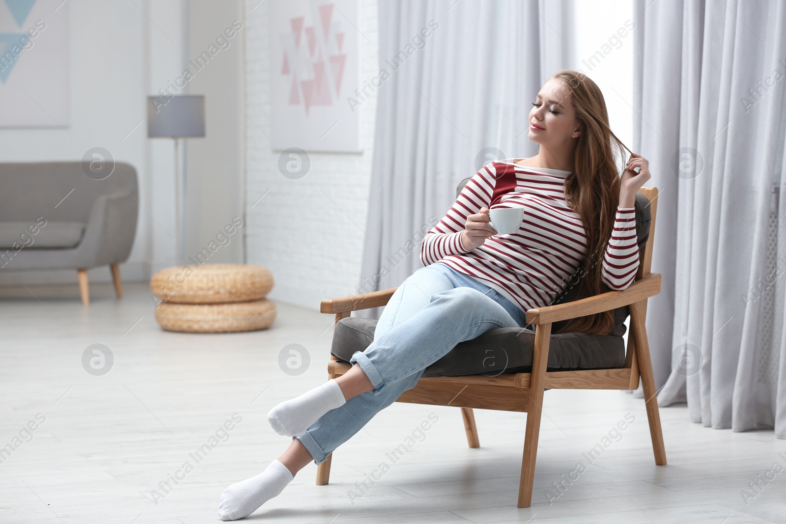 Photo of Young woman with cup of hot drink sitting in armchair at home. Space for text