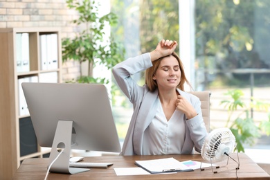 Businesswoman refreshing from heat in front of fan at workplace