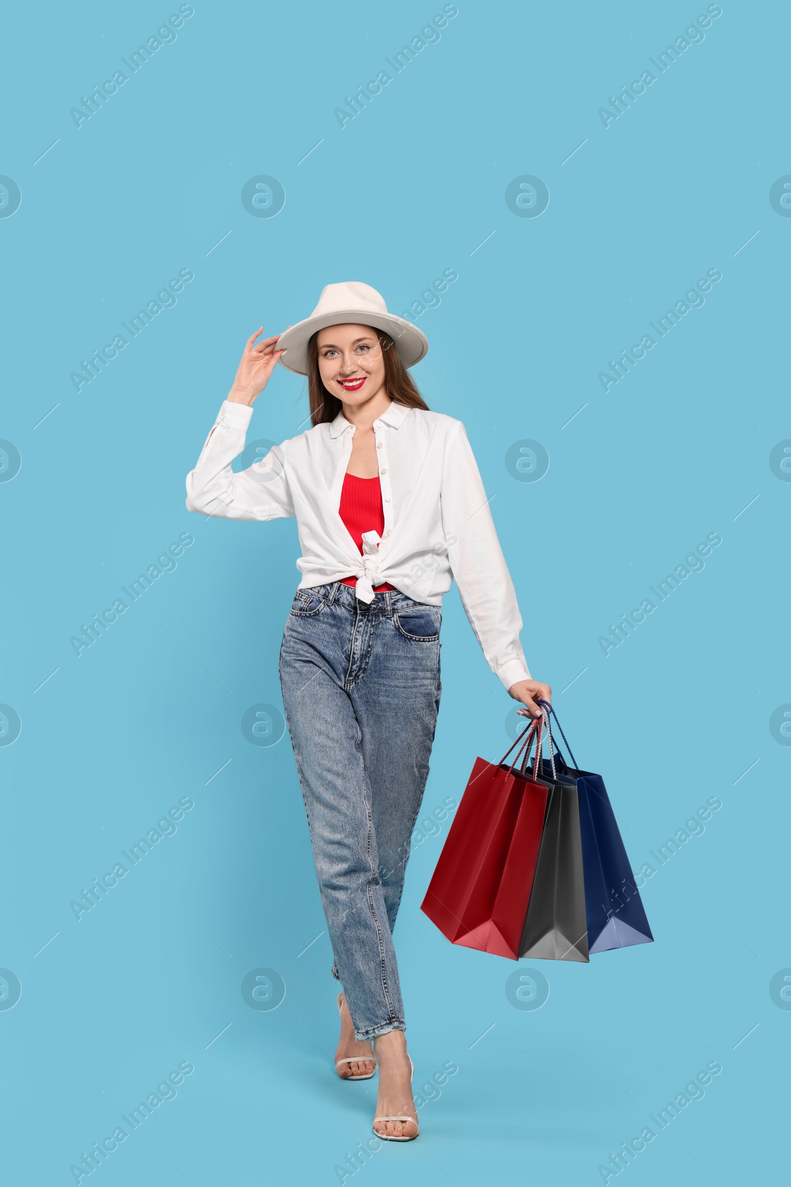 Photo of Stylish young woman with shopping bags on light blue background