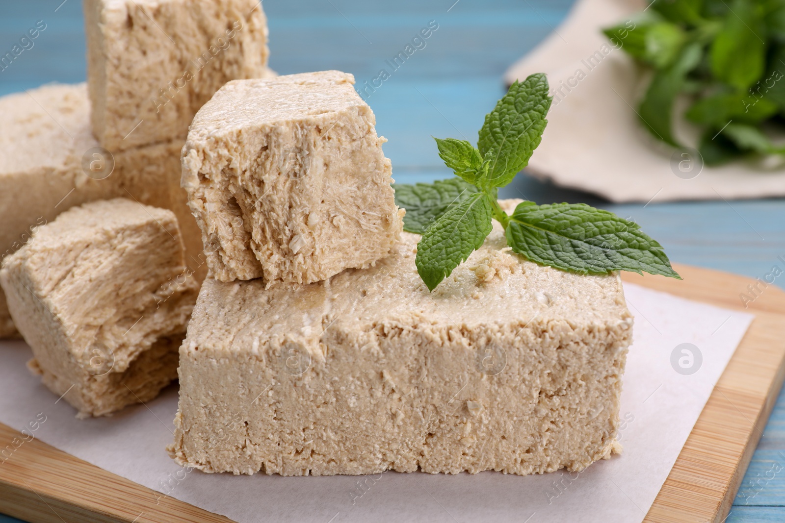 Photo of Pieces of tasty halva and mint on light blue table, closeup