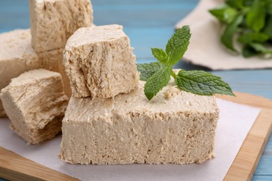 Pieces of tasty halva and mint on light blue table, closeup