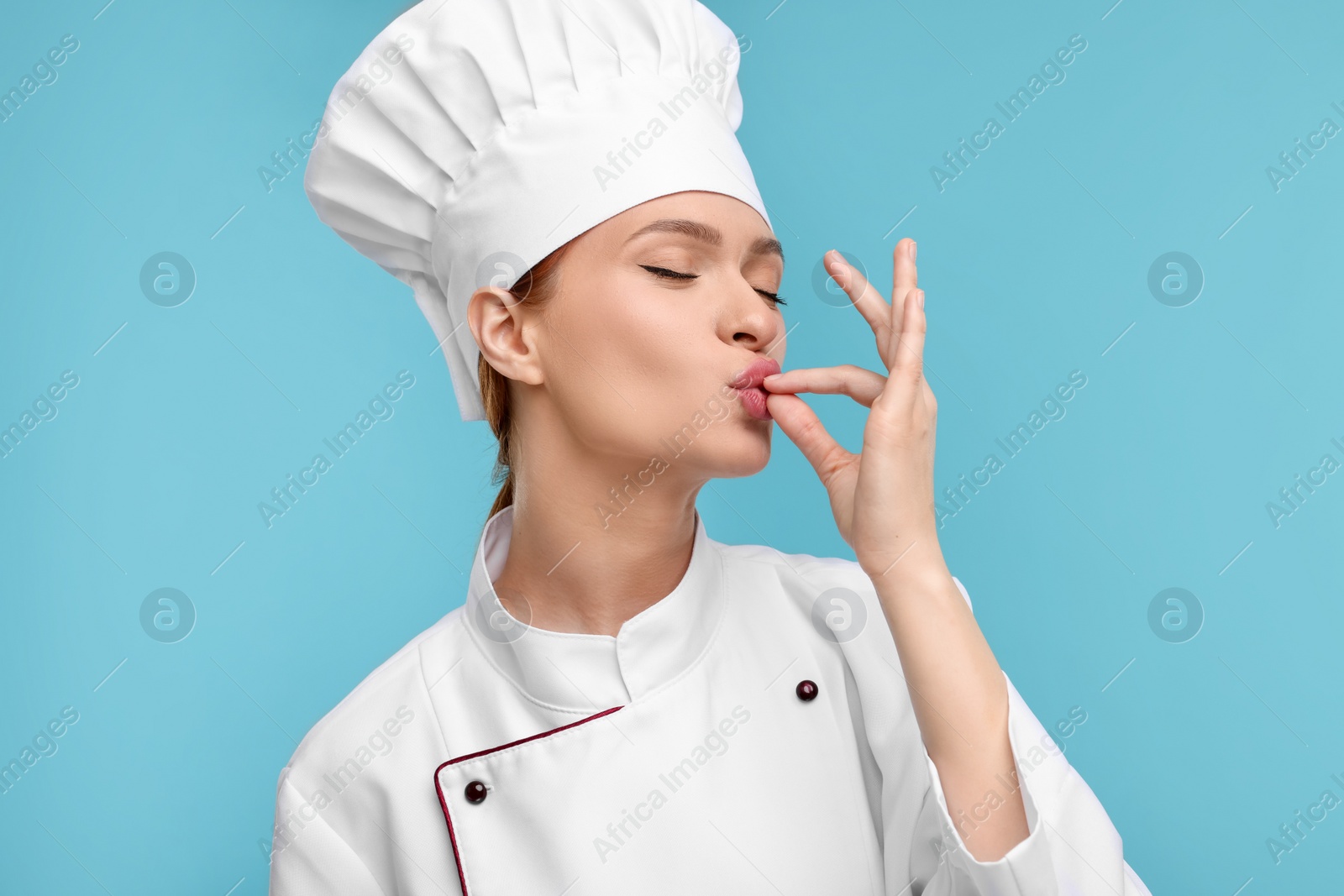 Photo of Happy woman chef in uniform showing perfect sign on light blue background