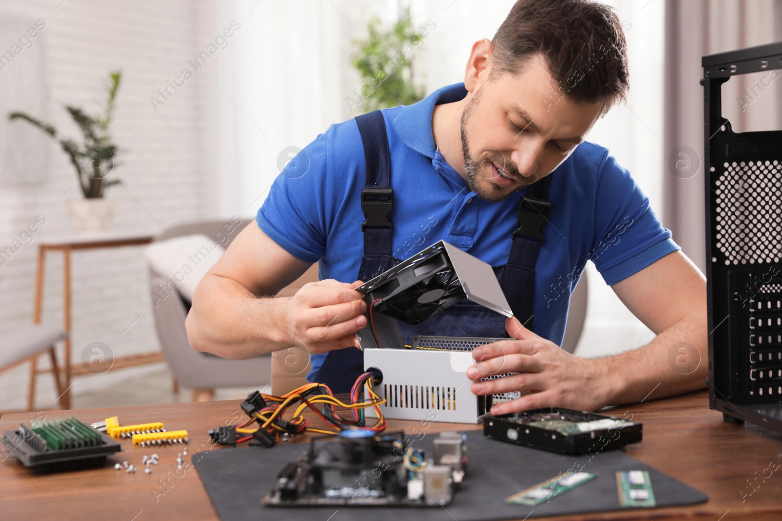 Photo of Male technician repairing power supply unit at table indoors