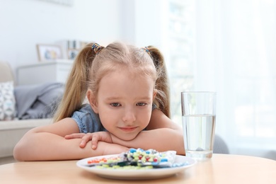 Photo of Little child with plate of different pills at home. Household danger