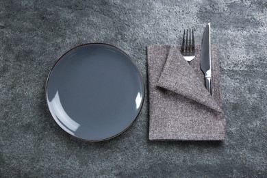 Photo of Ceramic plate, fork and knife wrapped in napkin on grey table, flat lay