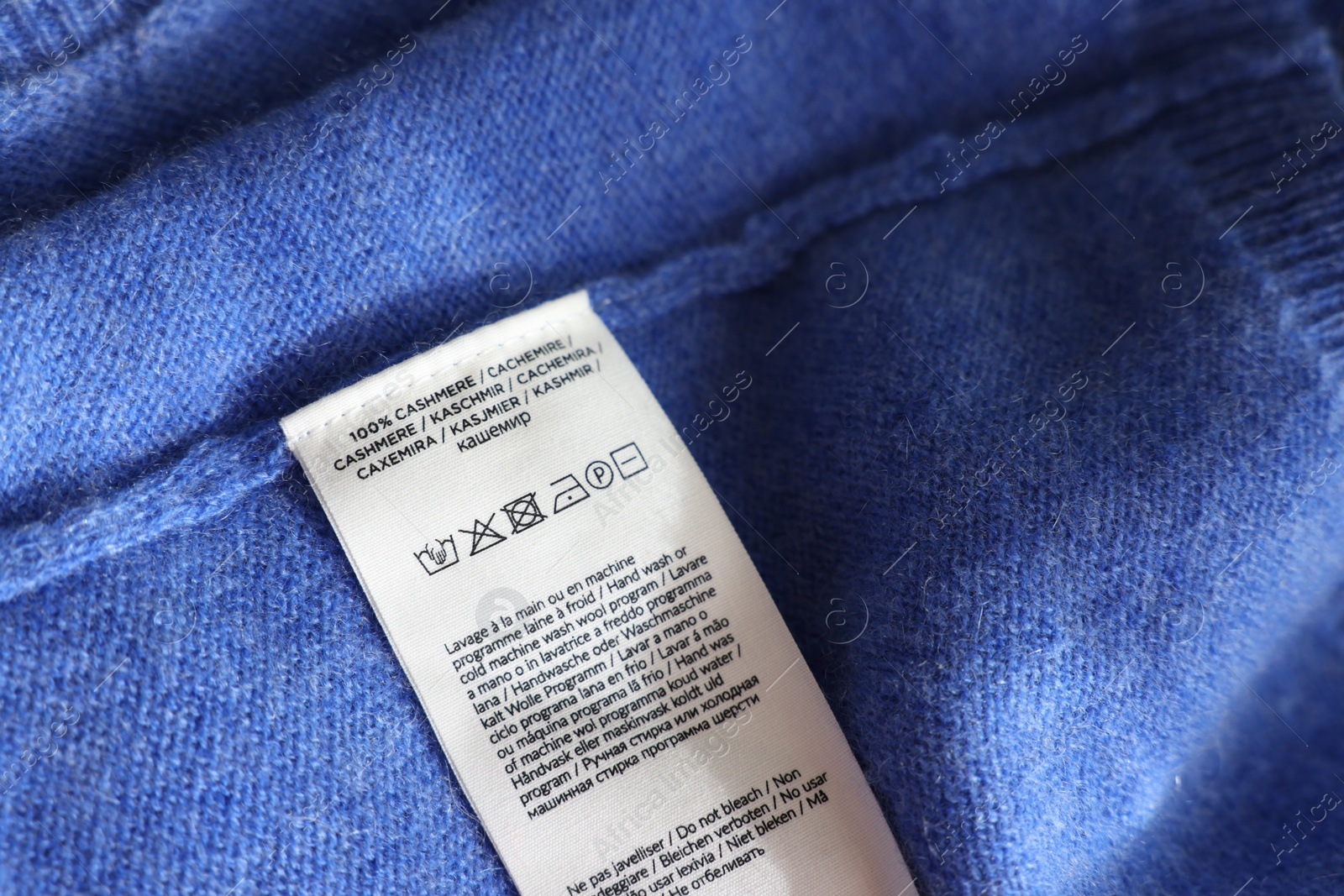 Photo of Clothing label in different languages on blue garment, closeup