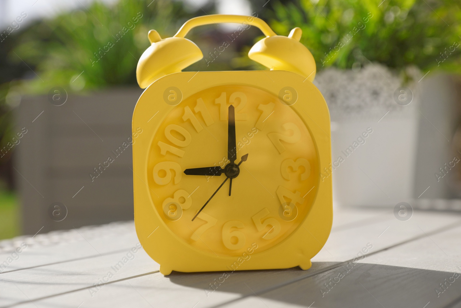 Photo of Yellow alarm clock on white wooden table outdoors at sunny morning