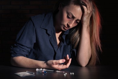Addicted woman at table with different drugs on black background