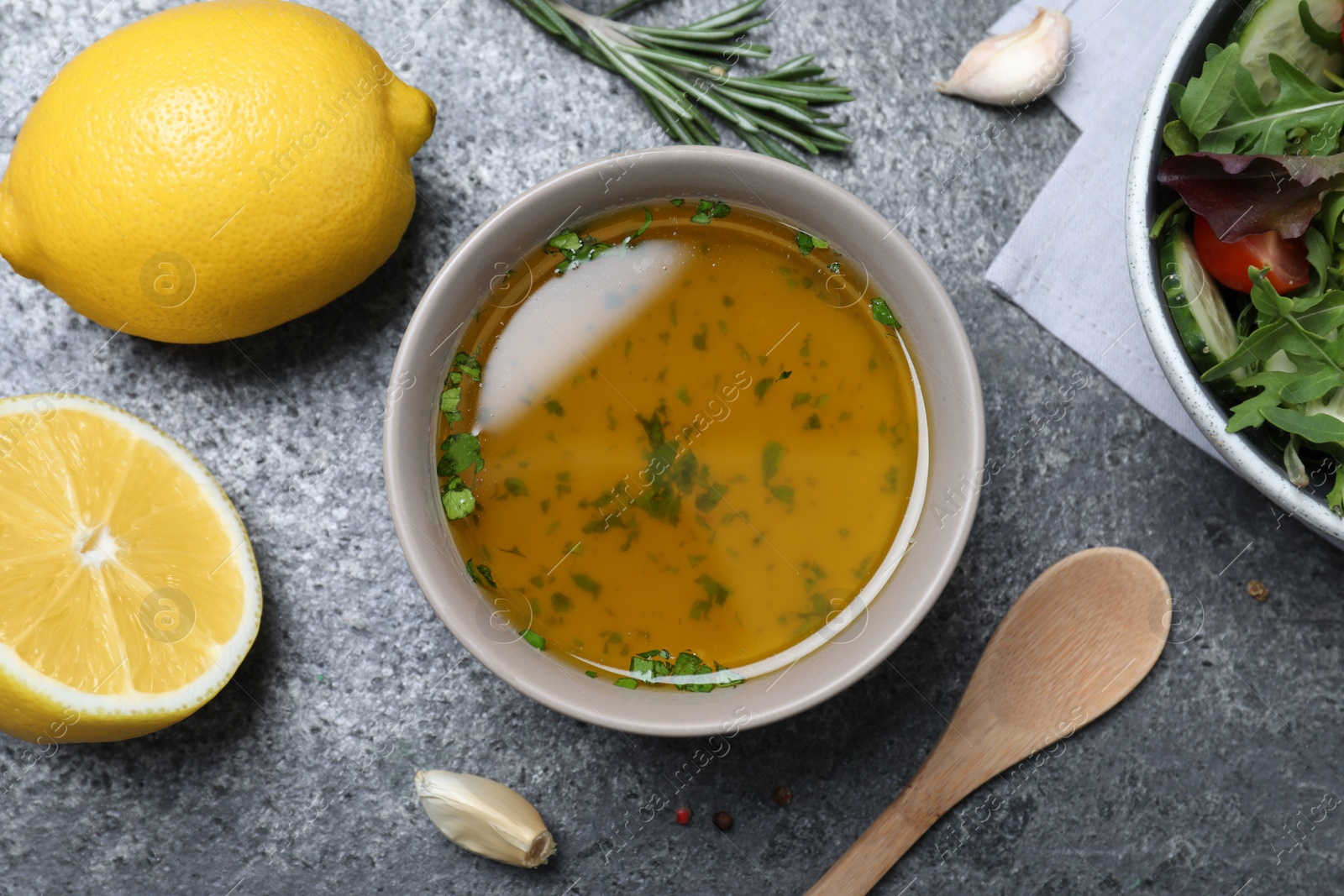 Photo of Bowl with lemon dressing near salad on grey table, flat lay. Delicious salad dressing