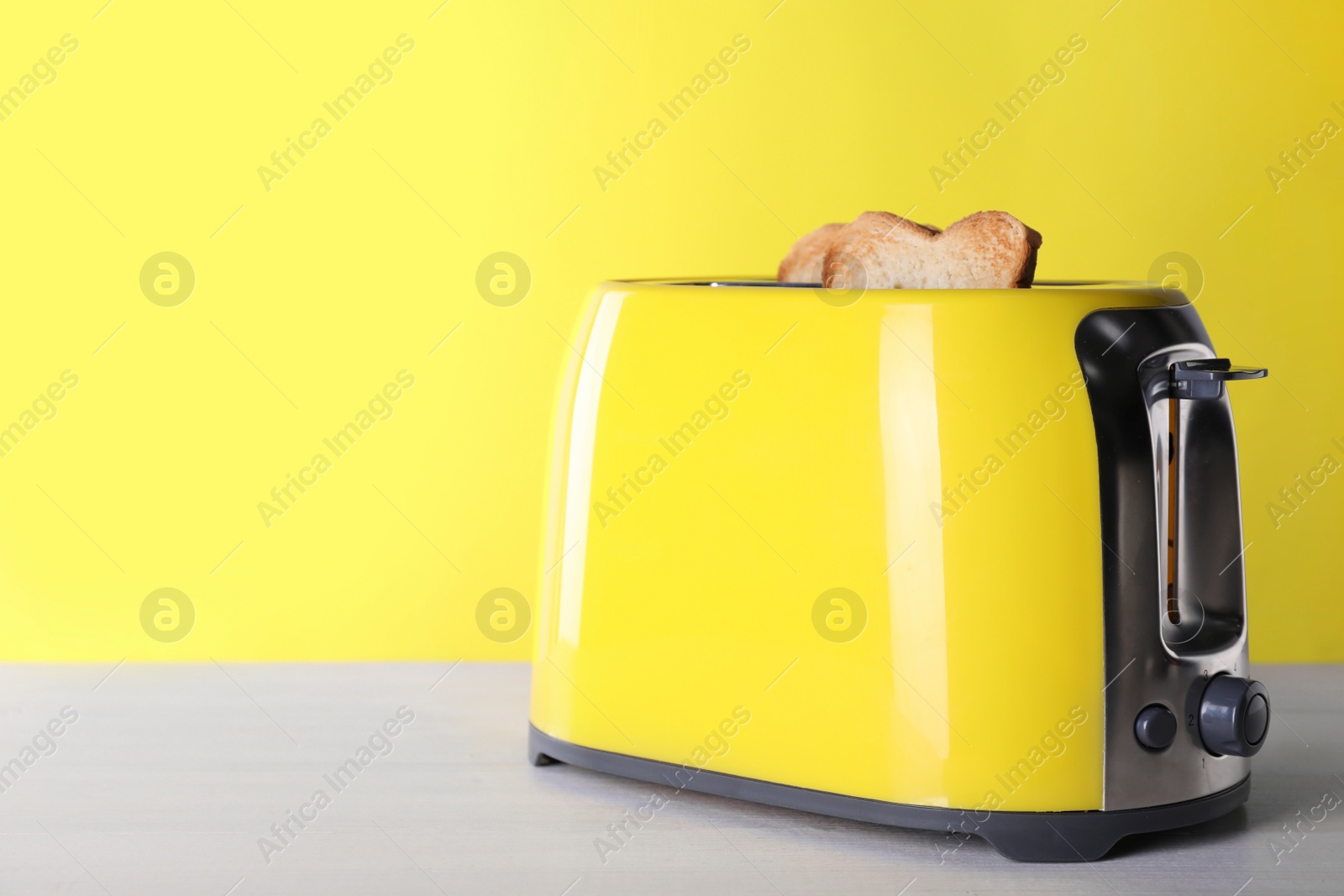 Photo of Modern toaster with slices of roasted bread on white wooden table. Space for text