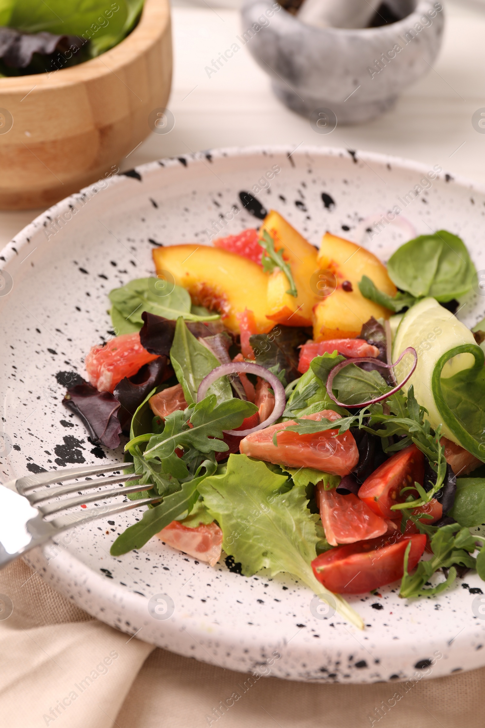 Photo of Delicious salad with vegetables and peach in bowl on table, closeup