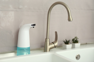 Photo of Modern automatic soap dispenser near sink indoors